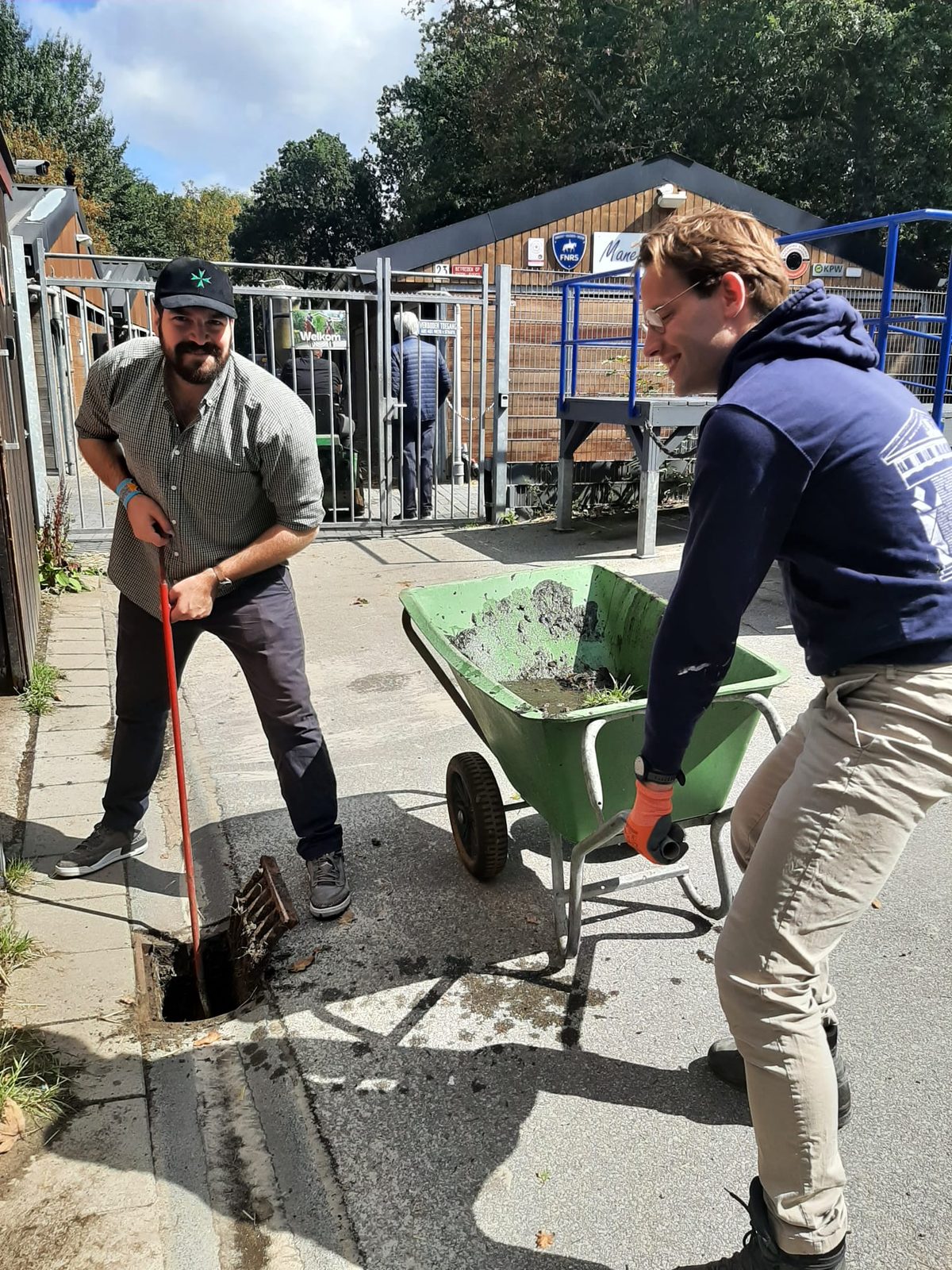 Twee deelnemers maken een straatkolk leeg boven een kruiwagen