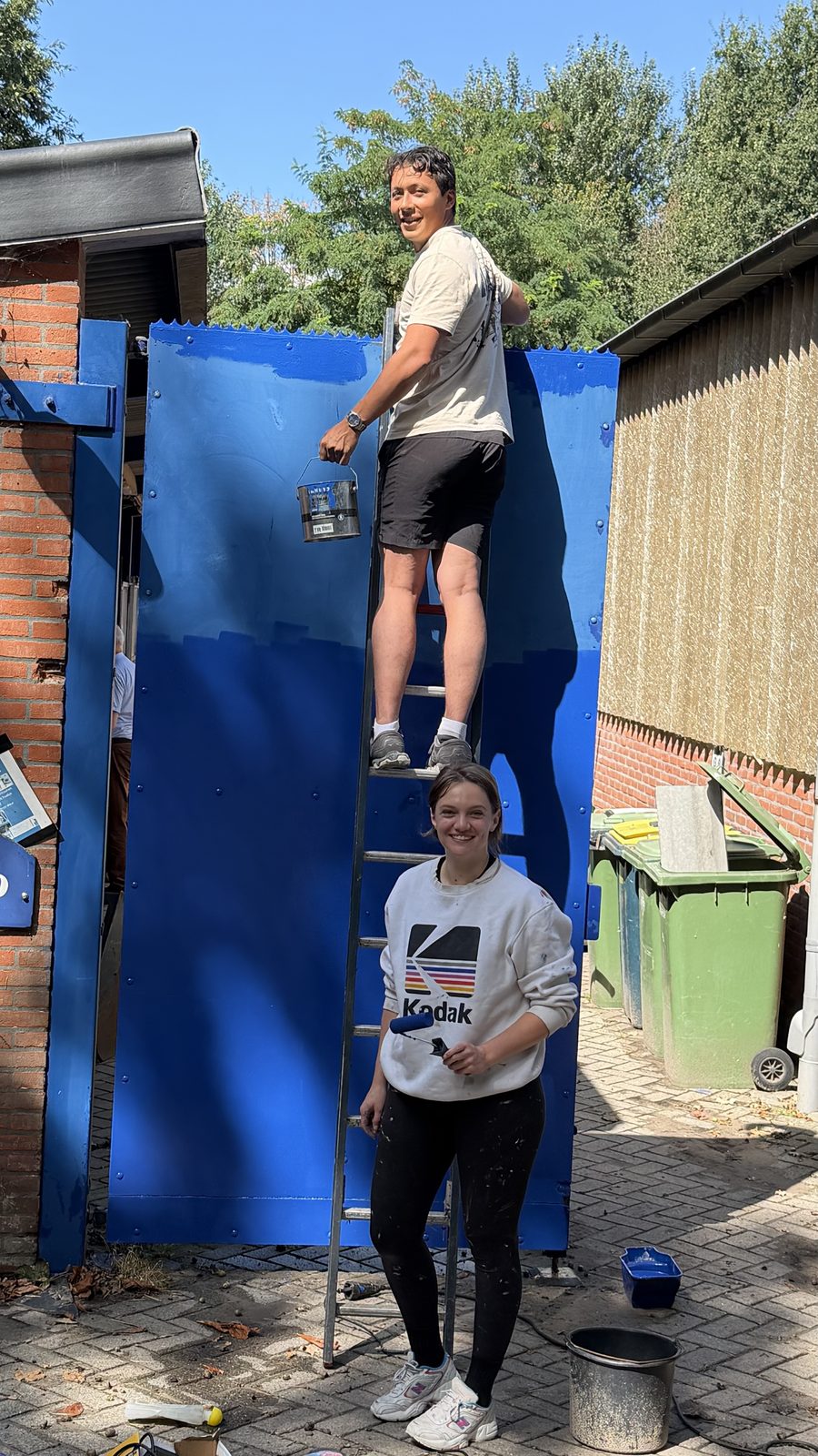 Twee deelnemers schilderen een poort in het blauw