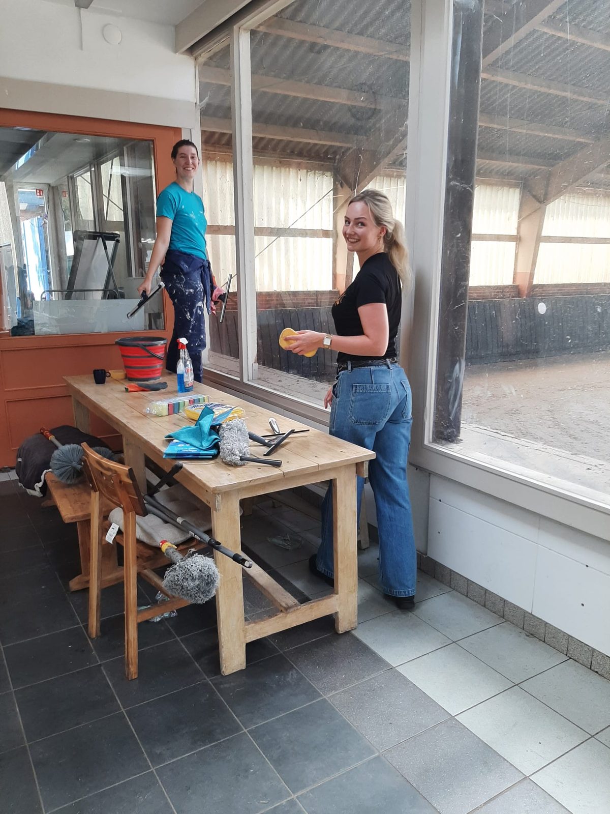 Twee deelnemers lappen de ramen van de kantine